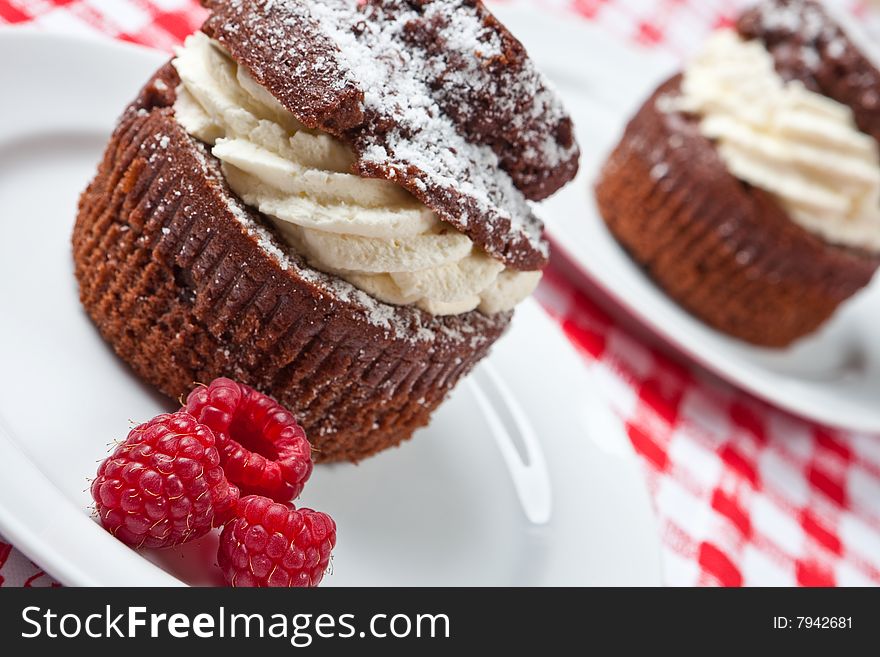 Delicious chocolate and cream muffins on a plate (focus on raspberries)