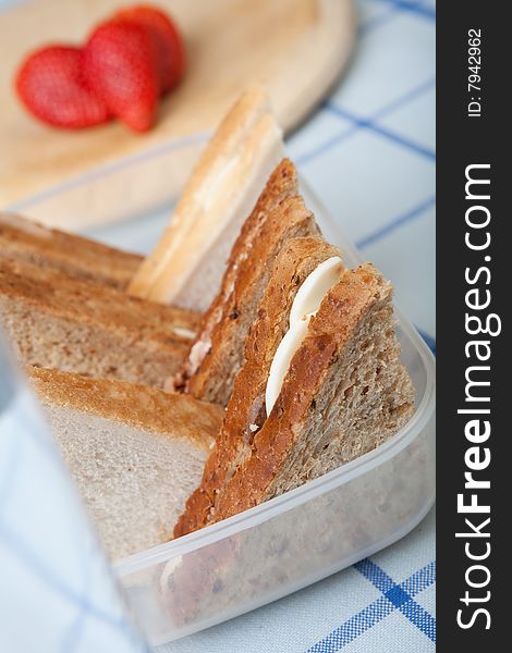 Fresh egg sandwiches in a lunch box with a strawberry in the background