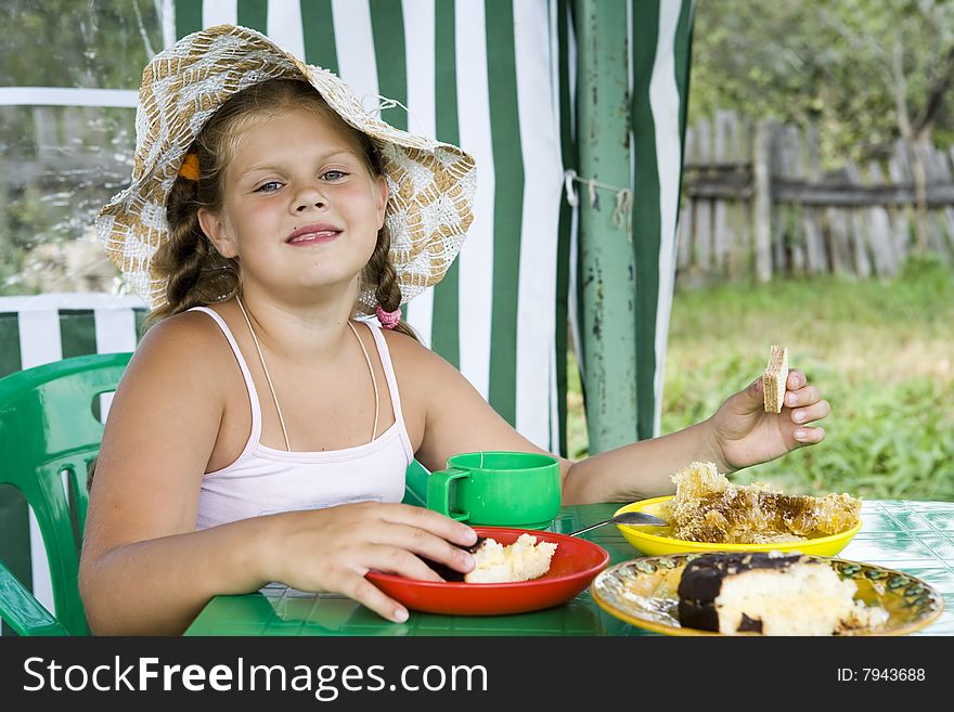 Little girl in big hat eats sweets and drinks tea
