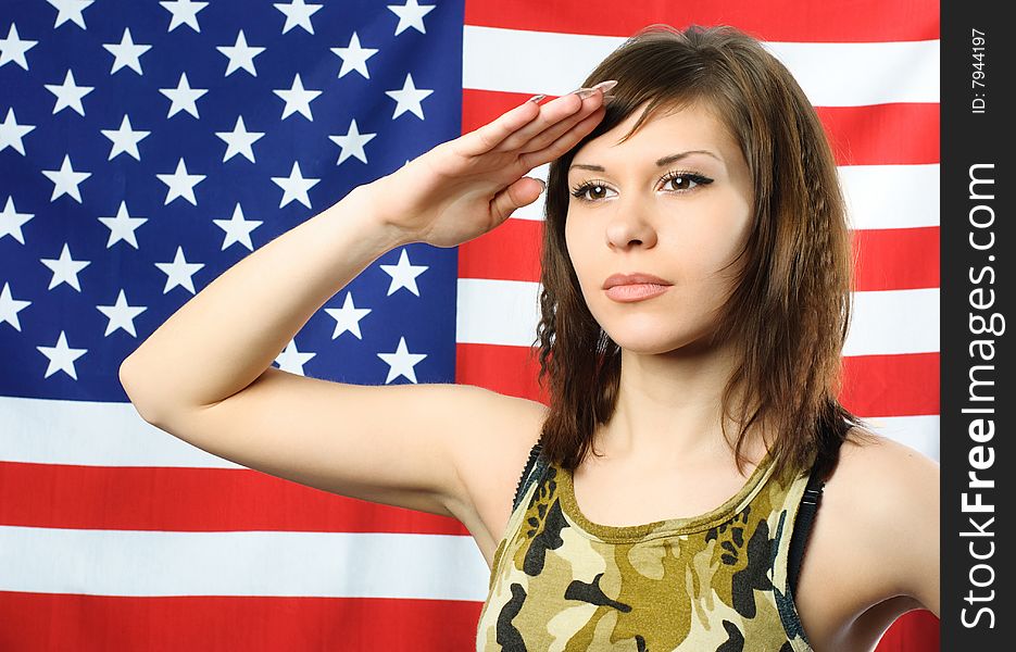 Beautiful young woman standing opposite an American flag and wearing camouflage salutes. Beautiful young woman standing opposite an American flag and wearing camouflage salutes