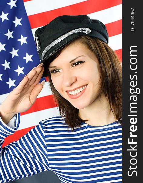 Happy beautiful young sailor stands near the American flag and salutes