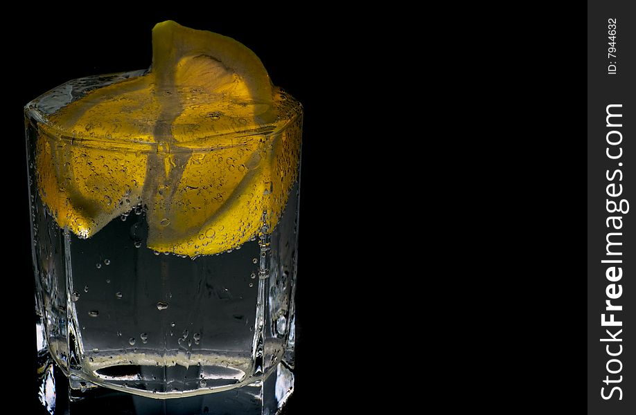 Glass with soda water and lemon slices on black background