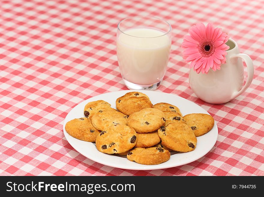 Plate of cookies with glass of milk and flower on checked tablecloth. Plate of cookies with glass of milk and flower on checked tablecloth.