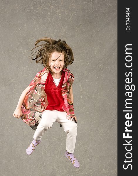 Little girl having fun leaping into air, over gray background. Little girl having fun leaping into air, over gray background