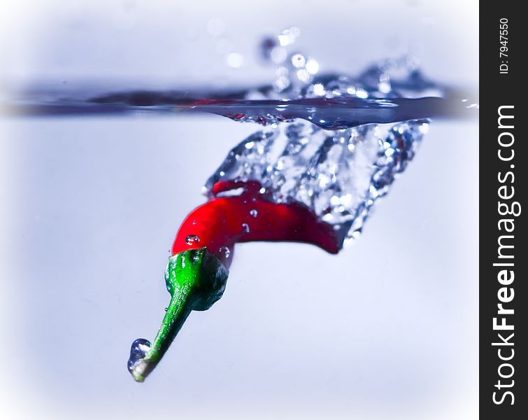A red chilli splashing into water.