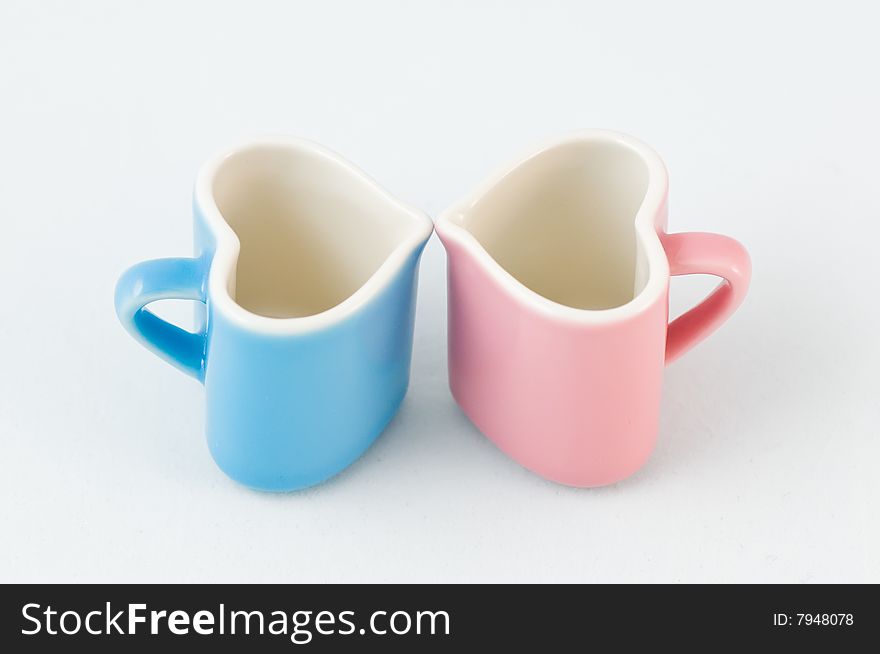 Two heart-shape blue and pink cups on white background with narrow depth of field. Two heart-shape blue and pink cups on white background with narrow depth of field