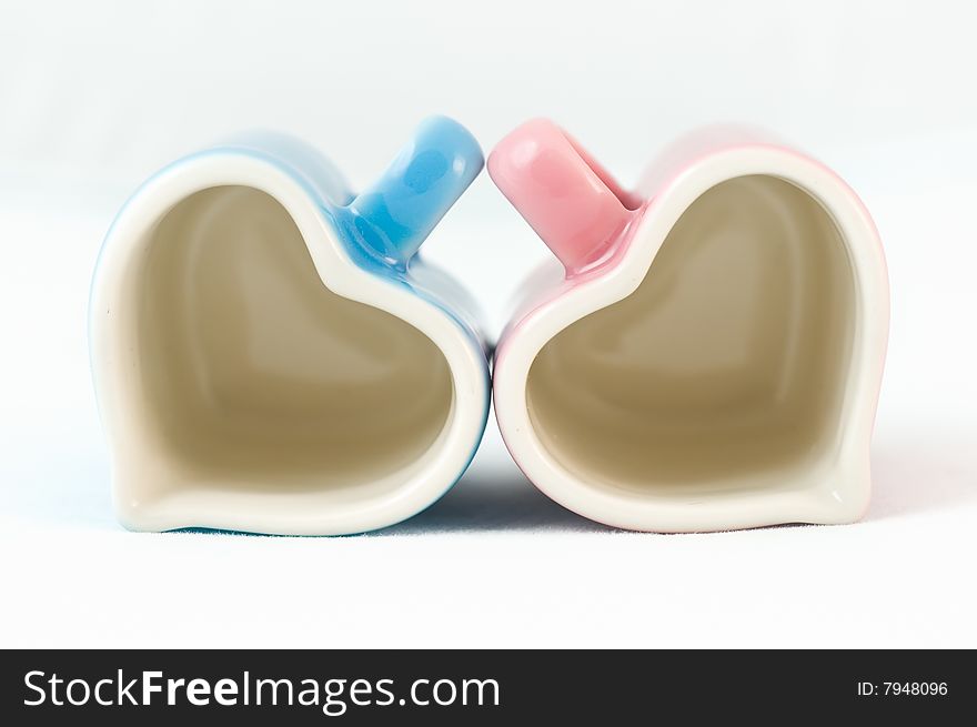 Two heart-shape blue and pink cups on white background with narrow depth of field. Two heart-shape blue and pink cups on white background with narrow depth of field