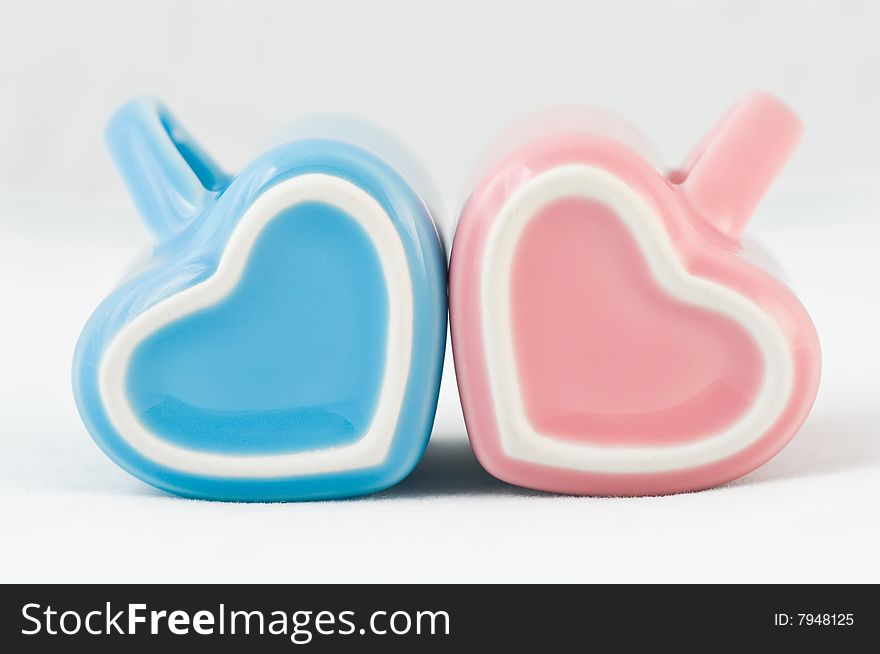 Two heart-shape blue and pink cups on white background with narrow depth of field. Two heart-shape blue and pink cups on white background with narrow depth of field