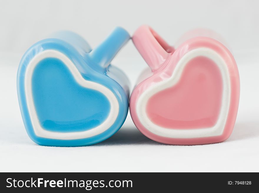 Two heart-shape blue and pink cups on white background with narrow depth of field. Two heart-shape blue and pink cups on white background with narrow depth of field