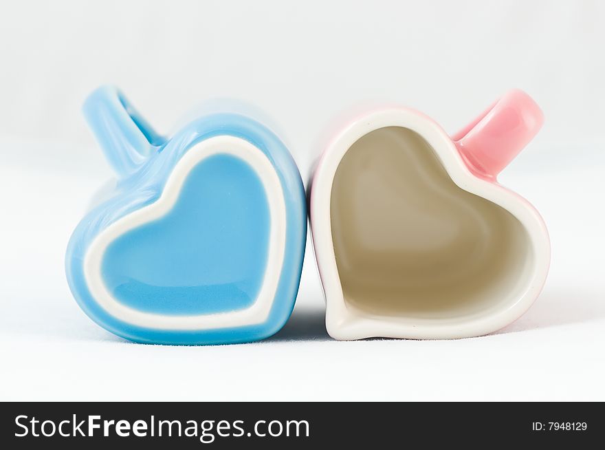 Two heart-shape blue and pink cups on white background with narrow depth of field. Two heart-shape blue and pink cups on white background with narrow depth of field