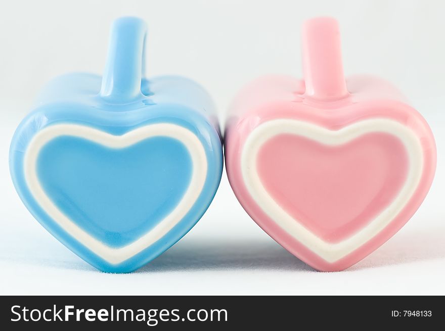 Two heart-shape blue and pink cups on white background with narrow depth of field. Two heart-shape blue and pink cups on white background with narrow depth of field
