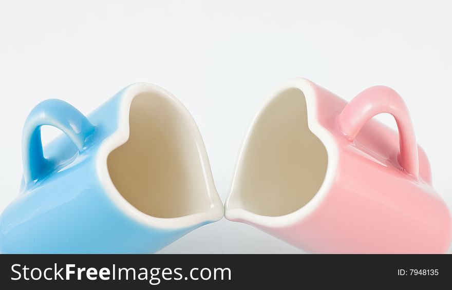 Two heart-shape blue and pink cups on white background with narrow depth of field. Two heart-shape blue and pink cups on white background with narrow depth of field