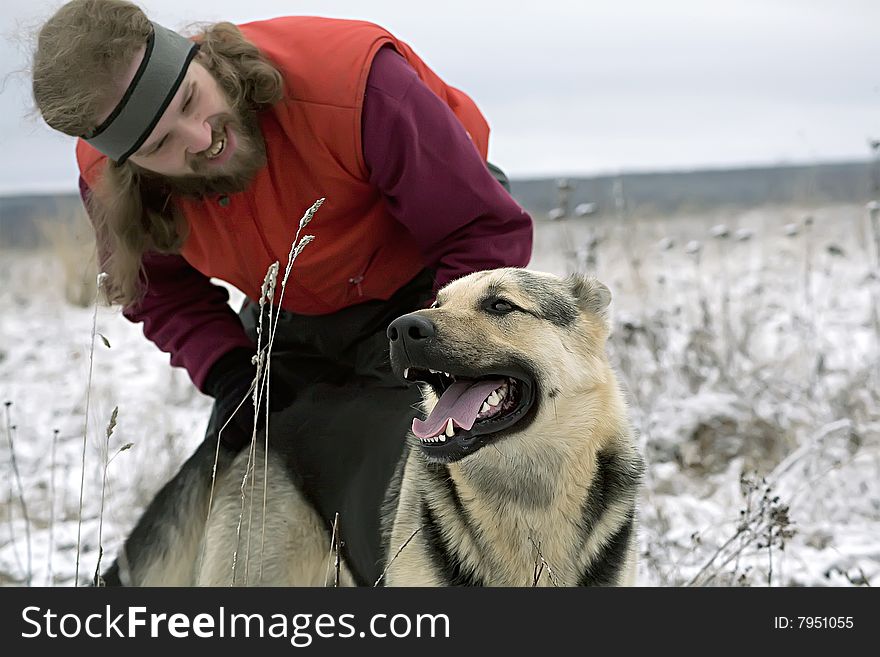 Smiling bearded man playing with alsatian dog in snowy meadow, winter, snow, forest in far away