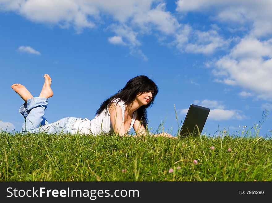 Pretty woman with laptop on the green grass