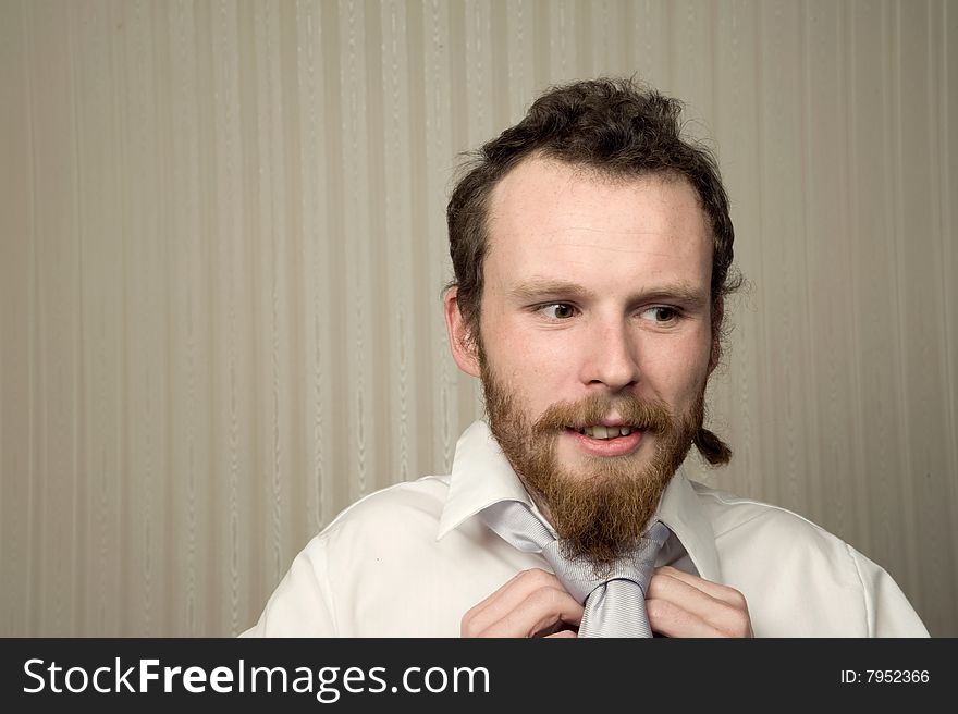 Young male with beard does up his tie with wallpaper behind. Young male with beard does up his tie with wallpaper behind