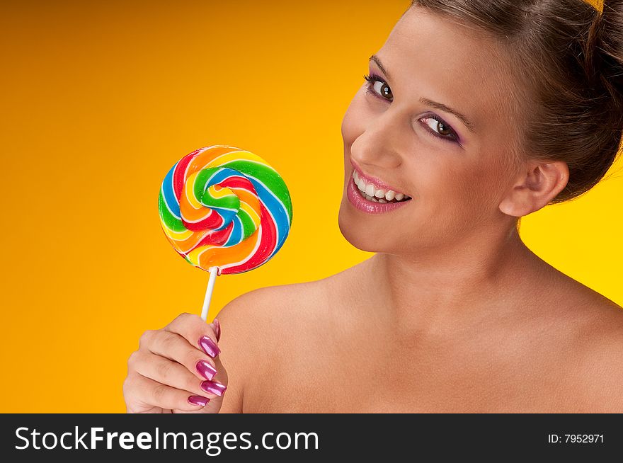 Smiling brunette woman with big lollipop on yellow background