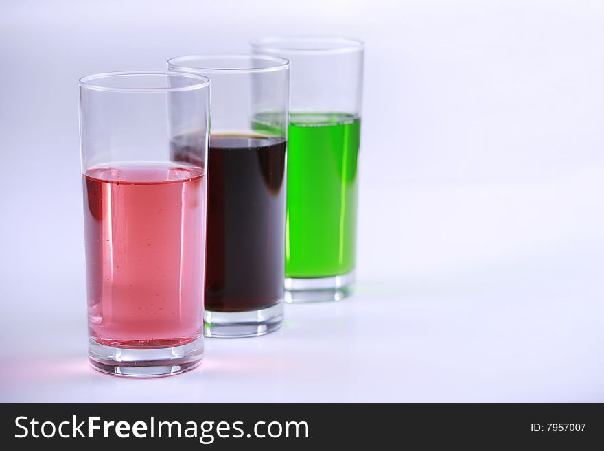 Three glasses with colorful drinks, side by side. blue tones in background
