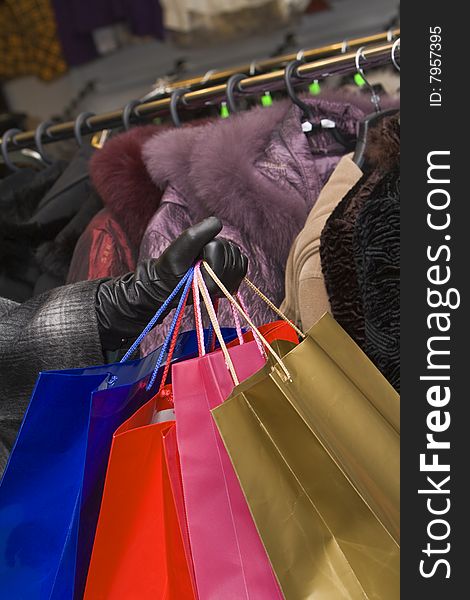 Hand holding a bunch of shopping bags in front of a clothes stall in a shop. Hand holding a bunch of shopping bags in front of a clothes stall in a shop.