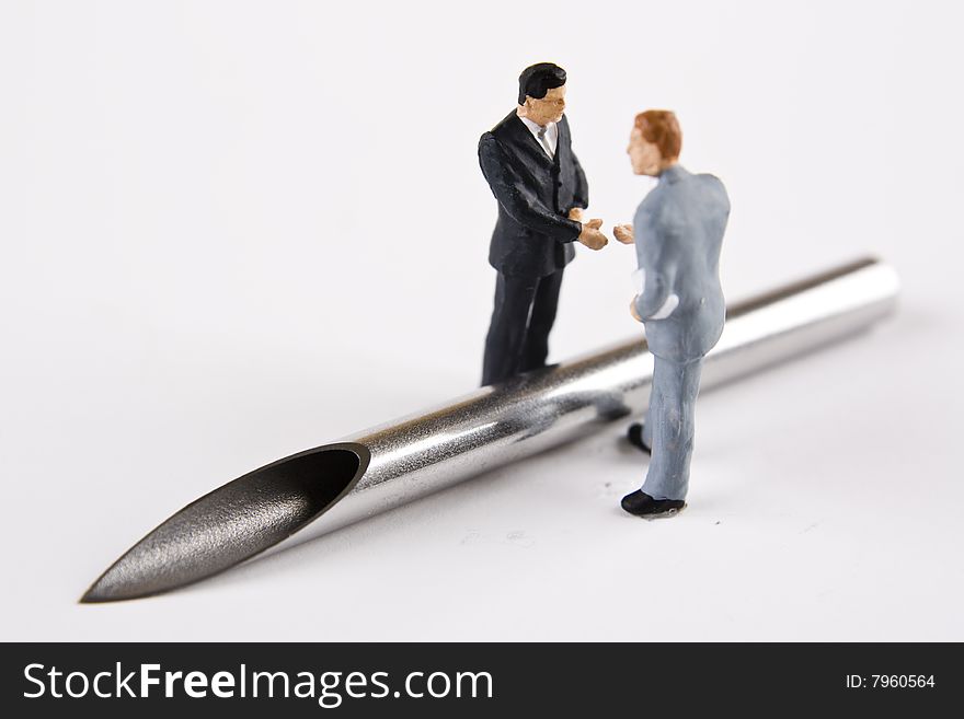 Miniature businessmen about to shake hands over a large bore needle. Miniature businessmen about to shake hands over a large bore needle.