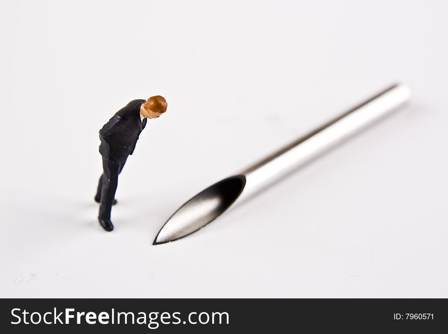 Miniature business man looking at the point of a piercing needle. Miniature business man looking at the point of a piercing needle.