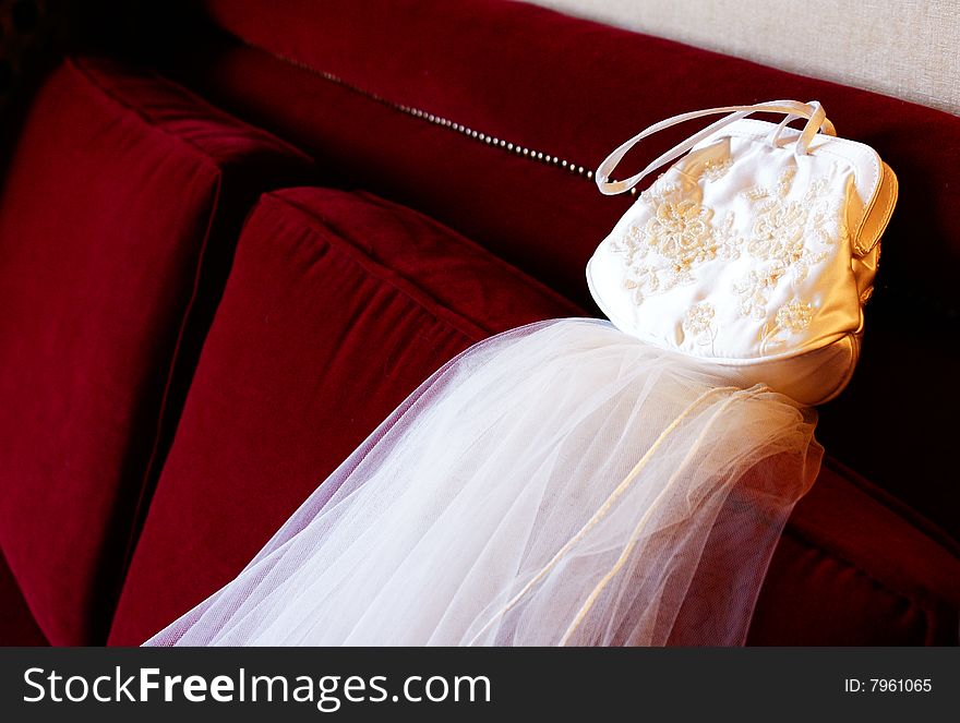 A white wedding purse resting on the veil on a red couch. A white wedding purse resting on the veil on a red couch