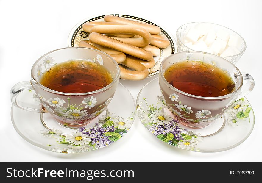 Two tea cups on a saucer with sugar and bagels