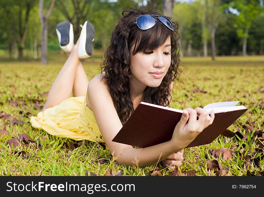 A young girl read a book in the outdoors. A young girl read a book in the outdoors