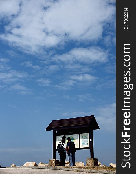 A couple looking direction in front of directories under blue sky and white clouds. A couple looking direction in front of directories under blue sky and white clouds