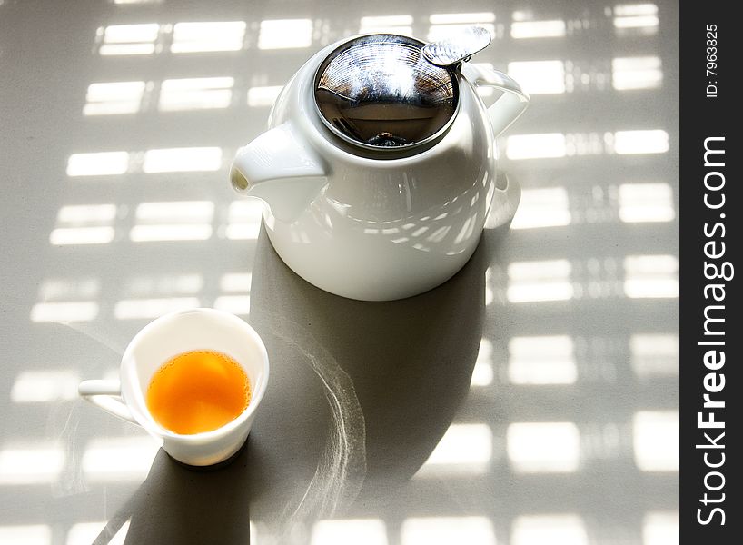 A picture of a cup of tea and a teapot basking under the sun. A picture of a cup of tea and a teapot basking under the sun