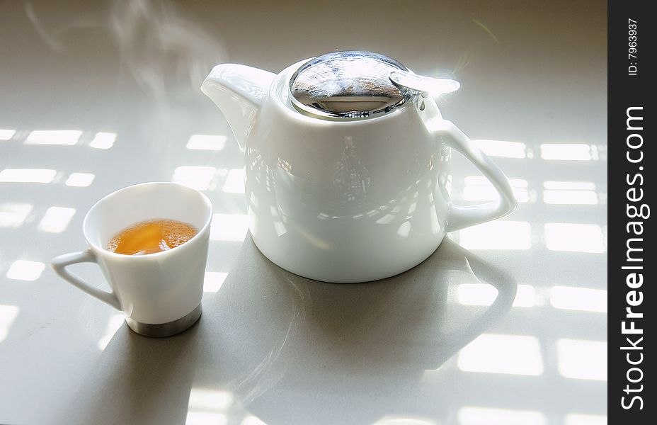 A picture of a cup of tea and a teapot basking under the sun. A picture of a cup of tea and a teapot basking under the sun