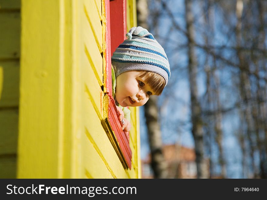 A child looking out from a widow of a colorful house at the playground. A child looking out from a widow of a colorful house at the playground