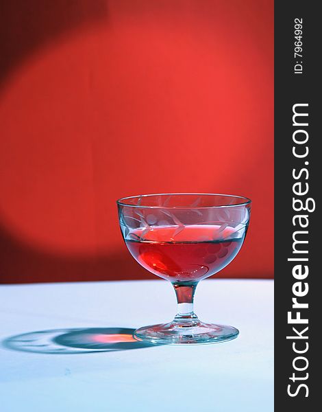 Photograph of a single glass of a red beverage on a red background.