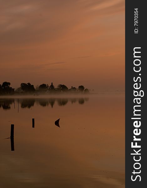 Dawn on a lake in northern holland. in the mist a fisherman is hauling in his nets. Dawn on a lake in northern holland. in the mist a fisherman is hauling in his nets.