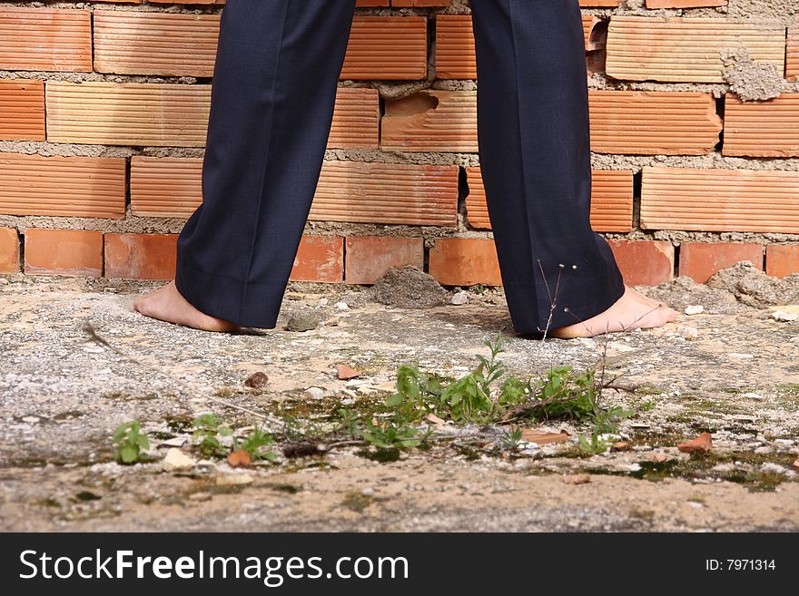 A businessman is standing barfoot in front of a brick wall. A businessman is standing barfoot in front of a brick wall