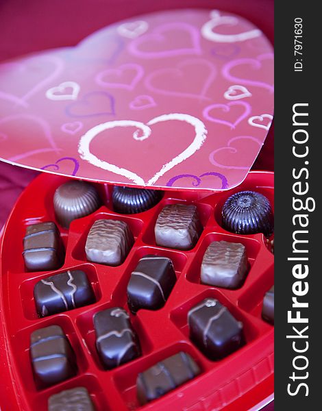 A box of chocolates is open with the top of the chocolate box on the outside rim of the pieces of chocolate. A box of chocolates is open with the top of the chocolate box on the outside rim of the pieces of chocolate