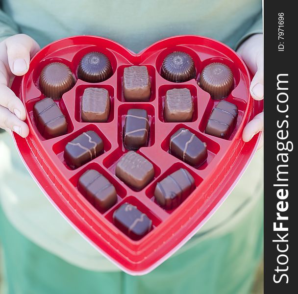 A boy is holding an open box of valentine's day chocolates in his hand up with the pieces of chocolate showing. A boy is holding an open box of valentine's day chocolates in his hand up with the pieces of chocolate showing