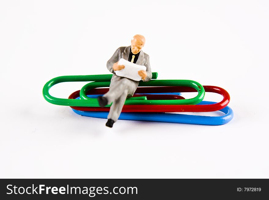 Miniature businessman sitting on paper clips. Miniature businessman sitting on paper clips
