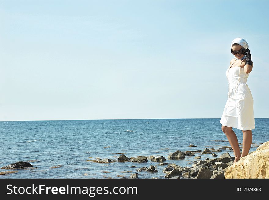 The beautiful young woman costs(stands) on a stone on a sea beach. The beautiful young woman costs(stands) on a stone on a sea beach