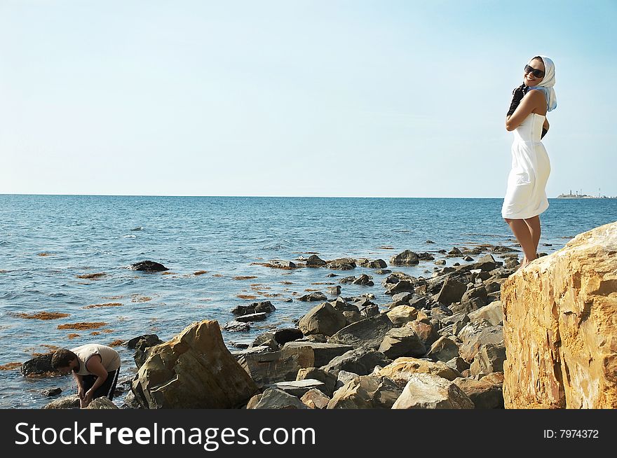 The beautiful young woman costs(stands) on a stone on a sea beach. The beautiful young woman costs(stands) on a stone on a sea beach