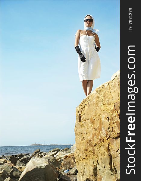 The beautiful young woman costs(stands) on a stone on a sea beach. The beautiful young woman costs(stands) on a stone on a sea beach