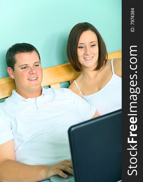 Young caucasian couple using laptop on their bed. Young caucasian couple using laptop on their bed