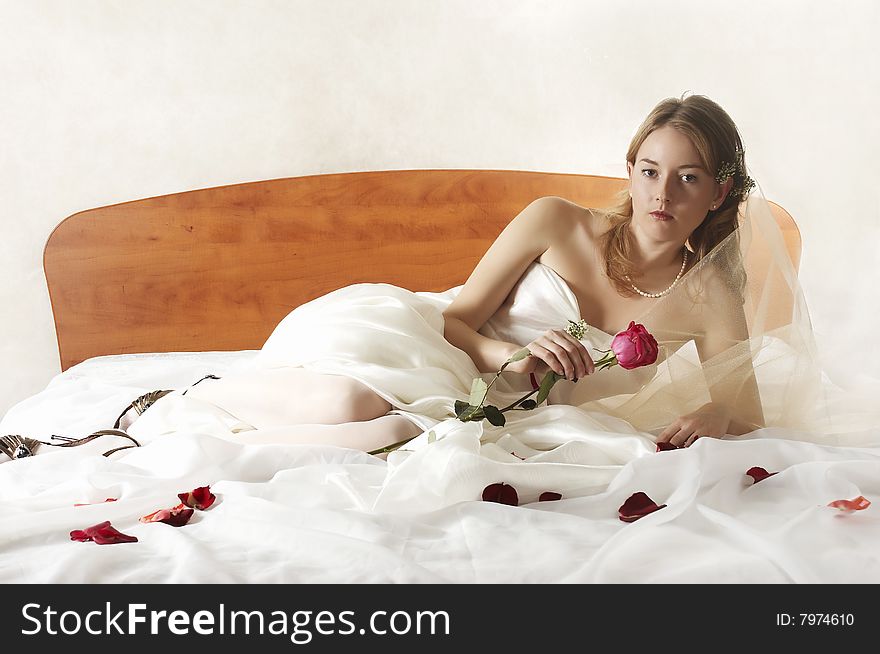 Bride lays on a bed with a red rose