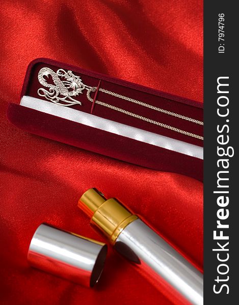 Silver necklace on a graceful chain and a bottle of perfume on a red drapery. Silver necklace on a graceful chain and a bottle of perfume on a red drapery.