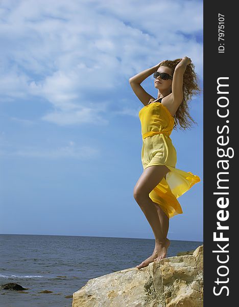 The beautiful young woman on a stone beach in a yellow dress. The beautiful young woman on a stone beach in a yellow dress