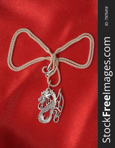 On a red drapery of a necklace a dragon on a silver chain. On a red drapery of a necklace a dragon on a silver chain.