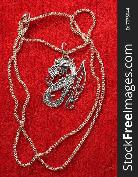 On a red drapery of a necklace a dragon on a silver chain. On a red drapery of a necklace a dragon on a silver chain.