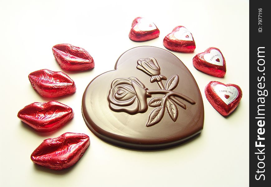 Heart and lips chocolates wrapped in red paper and a big heart chocolate with embossed flowers on it. Heart and lips chocolates wrapped in red paper and a big heart chocolate with embossed flowers on it