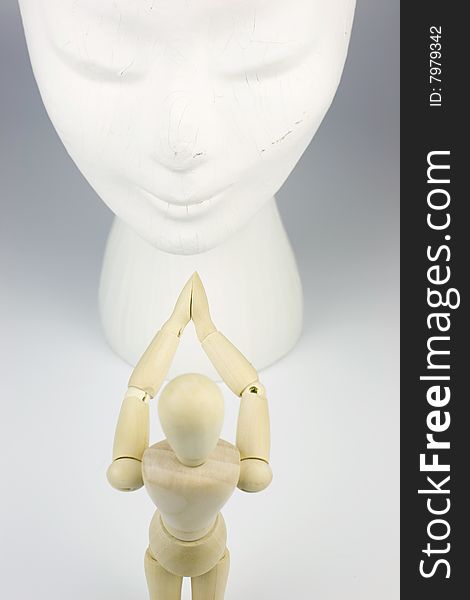 A wooden mannequin man praying to a white goddess face. A wooden mannequin man praying to a white goddess face.