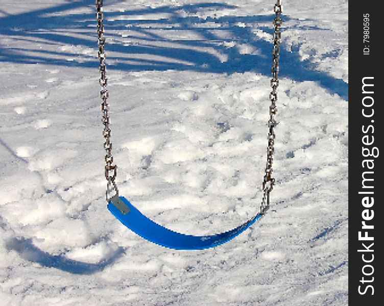 Blue swing hanging from metal or steel structure shadow shown in the background on the snow .  Foot prints of dogs and people all around.