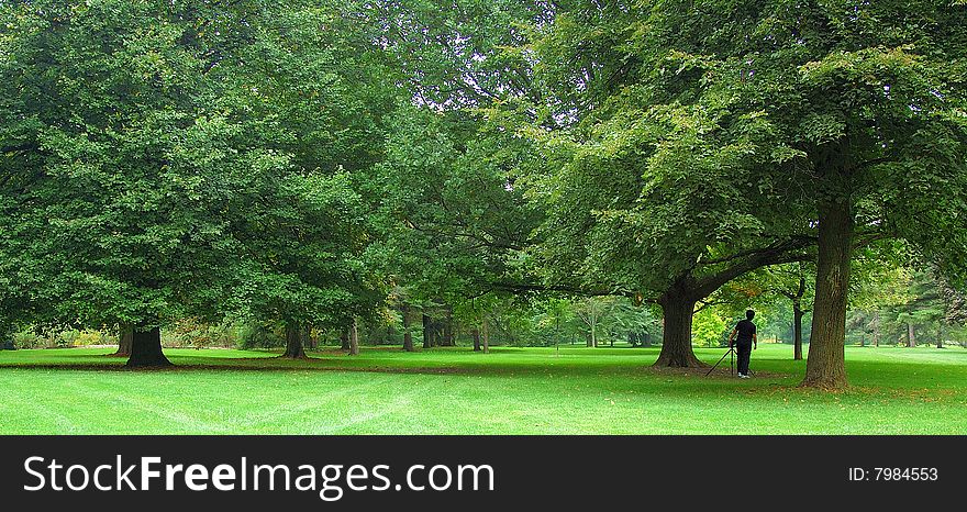 An image of a photographer in a distance scouting for a photography shoot in a beautiful lush green park. An image of a photographer in a distance scouting for a photography shoot in a beautiful lush green park.